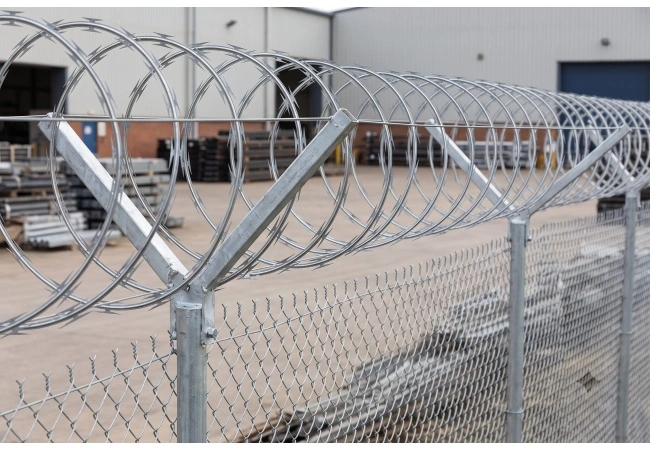 Concertina razor wire coils beside completed industrial perimeter fence showing relationship between coil product and supporting system